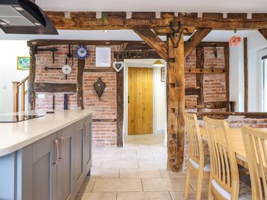 A kitchen and dining area with wooden beams exposed brick walls and a wooden dining table at Y Stabl The Stable in Llanrhaeadr-Ym-Mochnant