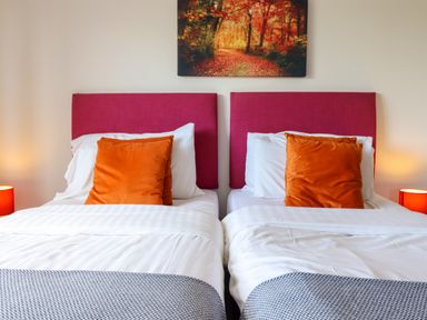A bedroom with two single beds with red headboards and orange pillows at Y Stabl (The Stable) in Llanrhaeadr-Ym-Mochnant