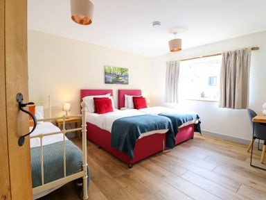 A bedroom with two single beds with red headboards and one single metal bed near a window with curtains at Y Stabl The Stable in Llanrhaeadr-Ym-Mochnant