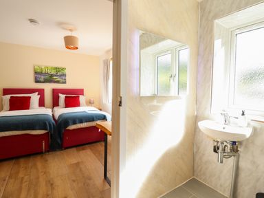 A bedroom with two single beds and a bathroom with a sink and mirror at Y Stabl The Stable in Llanrhaeadr-Ym-Mochnant