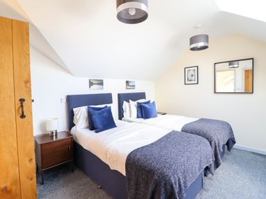 A bedroom with two single beds with blue headboards and pillows bedside tables with lamps a wooden door and framed pictures on the wall at Y Stabl The Stable in Llanrhaeadr-Ym-Mochnant