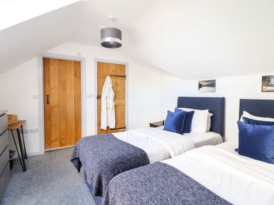 A bedroom with two single beds with blue headboards and pillows a wooden door a wooden closet door and a ceiling light at Y Stabl The Stable in Llanrhaeadr-Ym-Mochnant