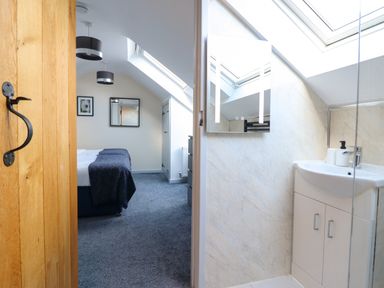 A bedroom with a bed and blue blanket next to a bathroom with a sink under skylights at Y Stabl The Stable in Llanrhaeadr-Ym-Mochnant