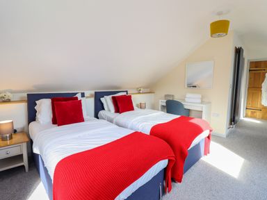 A bedroom with two single beds with red blankets and pillows a desk with a chair and a mirror at Y Stabl (The Stable) in Llanrhaeadr-Ym-Mochnant