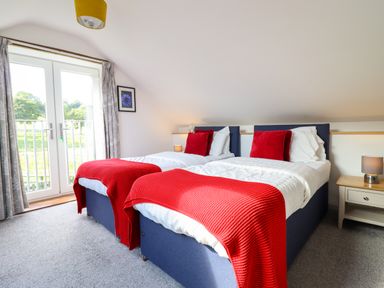 A bedroom with two single beds with red blankets and pillows next to a window at Y Stabl in Llanrhaeadr-Ym-Mochnant
