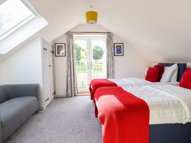 A bedroom with two beds red throws and pillows a gray sofa and double doors at Y Stabl The Stable in Llanrhaeadr-Ym-Mochnant