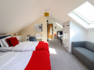 A bedroom with two single beds with red blankets a small desk with a chair a gray sofa and skylights at Y Stabl The Stable in Llanrhaeadr-Ym-Mochnant