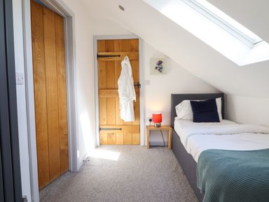 A bedroom with a single bed next to a wooden door and a small table with a lamp at Y Stabl The Stable in Llanrhaeadr Ym Mochnant
