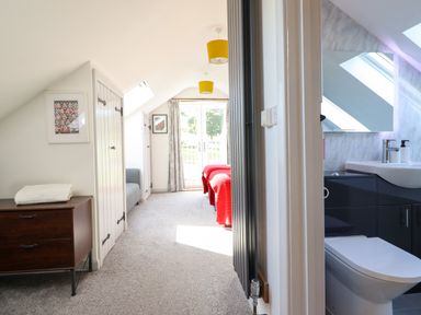 A bedroom with two beds covered with red blankets next to a bathroom with a toilet and sink at Y Stabl The Stable in Llanrhaeadr-Ym-Mochnant
