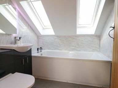 A bathroom with a bathtub under skylight windows and a sink with cabinet at Y Stabl Llanrhaeadr-Ym-Mochnant