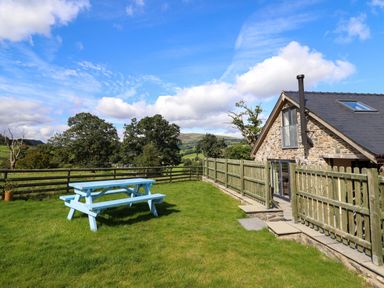 A stone cottage with a fenced garden and a blue picnic table on the grass at Y Stabl The Stable in Llanrhaeadr-Ym-Mochnant