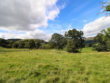 A grassy field with trees and hills under a partly cloudy sky at Y Stabl (The Stable) in Llanrhaeadr-Ym-Mochnant