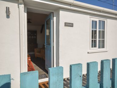 An open door with a blue frame leading into a room with a chair and cabinet behind a blue wooden fence at Ffrwd in Rhosneigr