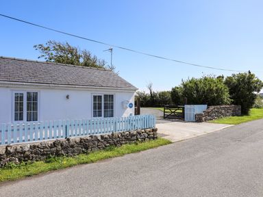 A white house with two windows a light blue fence a stone wall and a driveway gate at Ffrwd in Rhosneigr