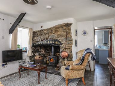 A living room with a stone fireplace wood burning stove an armchair a coffee table and a television at Ffrwd in Rhosneigr