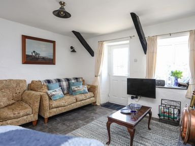 A living room with patterned sofas a wooden coffee table a wall mounted TV and a painting at Ffrwd in Rhosneigr