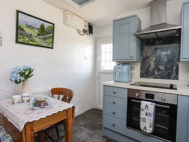 A kitchen with blue cabinets a wooden table with two cups and a cake and a door with a window at Ffrwd in Rhosneigr