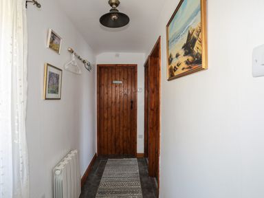 A hallway with a wooden door a rug on the floor paintings on the walls and a light fixture on the ceiling at Ffrwd in Rhosneigr