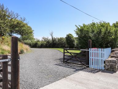 A gravel driveway with wooden gates and green trees around at Ffrwd in Rhosneigr