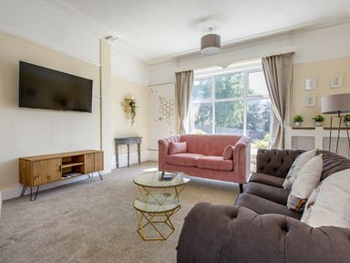 A living room with a pink sofa a grey sofa a wooden TV stand with a TV on the wall and a large window at Sunnymeade in Buxton Norfolk