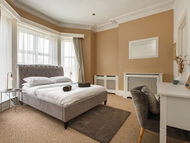 A bedroom with a bed a desk chair side table and windows with sheer curtains at Sunnymeade in Buxton Norfolk