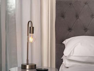 A bedside table with a lamp and a bed with a pillow and tufted headboard at Sunnymeade in Buxton Norfolk