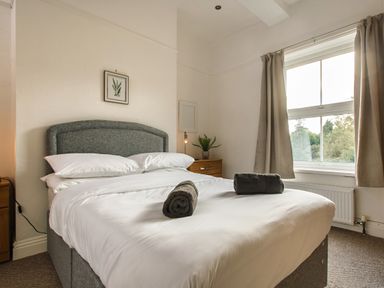 A bedroom with a double bed white bedding rolled towels bedside table with plant window with curtains at Sunnymeade in Buxton Norfolk