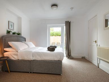 A bedroom with a grey bed white bedding and towels on the bed next to a glass door and a small round table at Sunnymeade in Buxton Norfolk