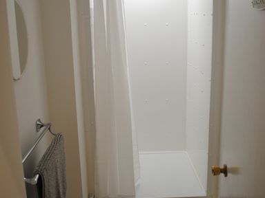 A bathroom shower area with a white shower curtain and a gray towel on a metal towel rack at Sunnymeade in Buxton Norfolk
