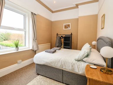 A bedroom with a bed two folded towels a bedside table with a lamp a window with curtains a plant and a clothes rack at Sunnymeade in Buxton Norfolk