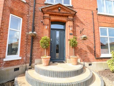 A front entrance with a dark door two potted plants on steps and red brick walls at Sunnymeade in Buxton Norfolk