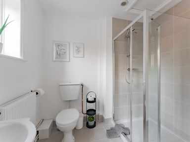 A bathroom with a toilet a glass shower enclosure and framed pictures on the wall at Sunnymeade in Buxton Norfolk