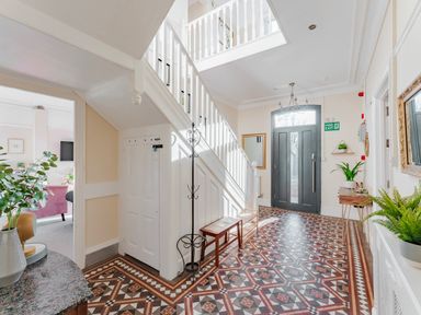 An entrance hallway with tiled floor a dark front door a staircase with white balustrades and various plants at Sunnymeade in Buxton Norfolk