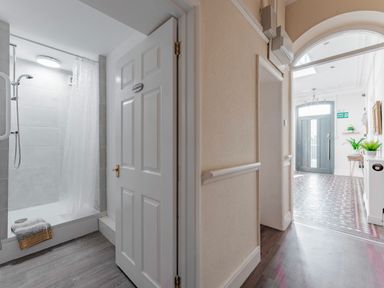 A hallway leading to a shower room with a white door and a gray tiled shower at Sunnymeade in Buxton Norfolk