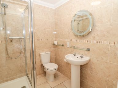 A bathroom with a shower enclosure toilet pedestal sink and round mirror at Jubilee House in Embleton