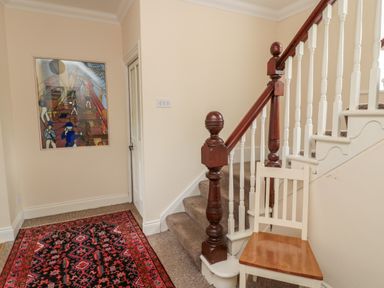 A staircase with wooden banister and a chair beside a red patterned rug on a carpeted floor at Jubilee House in Embleton