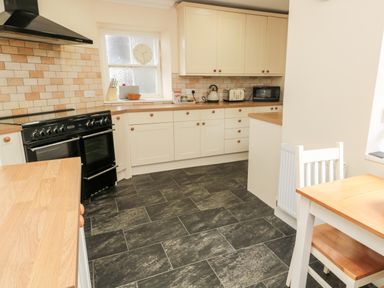A kitchen with black stove white cabinets wooden countertops and a wooden table with chair at Jubilee House in Embleton