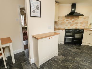 A kitchen with cream cabinets a black stove and a tiled backsplash at Jubilee House in Embleton
