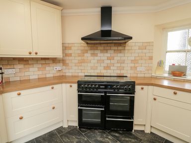 A kitchen with cream cabinets a black stove and a tiled backsplash at Jubilee House in Embleton