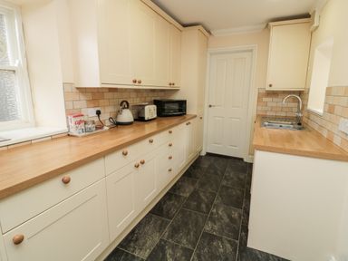A kitchen with countertops cabinets a microwave toaster kettle sink and tiled floor at Jubilee House in Embleton