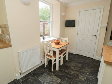 A small dining area with a wooden table and two chairs near a window and a wall-mounted TV at Jubilee House in Embleton