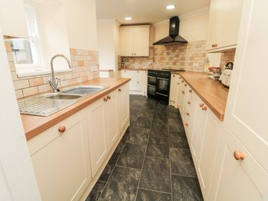 A galley kitchen with wooden countertops white cabinets a black stove and a stainless steel sink at Jubilee House in Embleton
