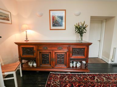 A wooden sideboard with decorative carvings a lamp and flowers on top and crockery below at Jubilee House in Embleton