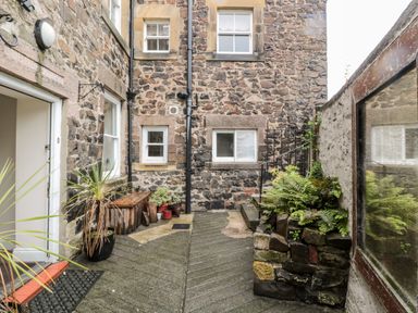 A stone-walled courtyard with potted plants a wooden bench and stairs at Jubilee House in Embleton
