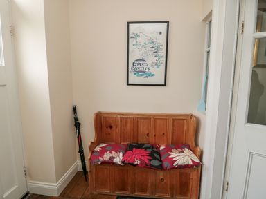A wooden bench with three floral cushions an umbrella in the corner and a framed map on the wall at Jubilee House in Embleton