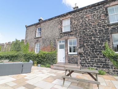 An outdoor patio area with stone paving furniture and a wooden picnic table outside a stone house with ivy growing on the walls at Jubilee House in Embleton