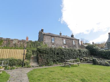 An outdoor garden area with grass a wooden picnic table stone steps leading up to a stone house with ivy on the walls at Jubilee House in Embleton