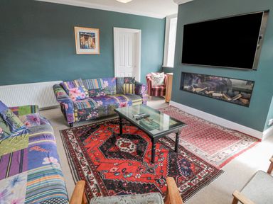 A living room with patterned sofas a glass coffee table a wall-mounted TV and a fireplace at Jubilee House in Embleton
