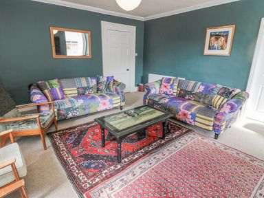 A living room with two patterned sofas a wooden armchair a coffee table and two rugs at Jubilee House in Embleton