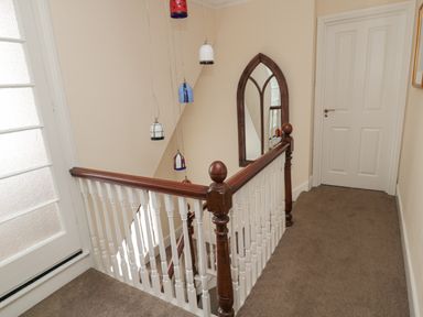 A staircase landing with wooden railing a white door a mirror on the wall and hanging pendant lights at Jubilee House in Embleton